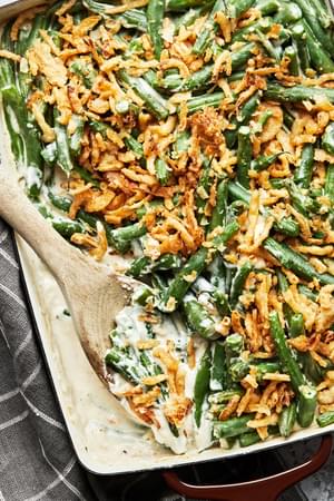 homemade green bean casserole with a creamy sauce and topped with French fried onions being scooped from a casserole dish