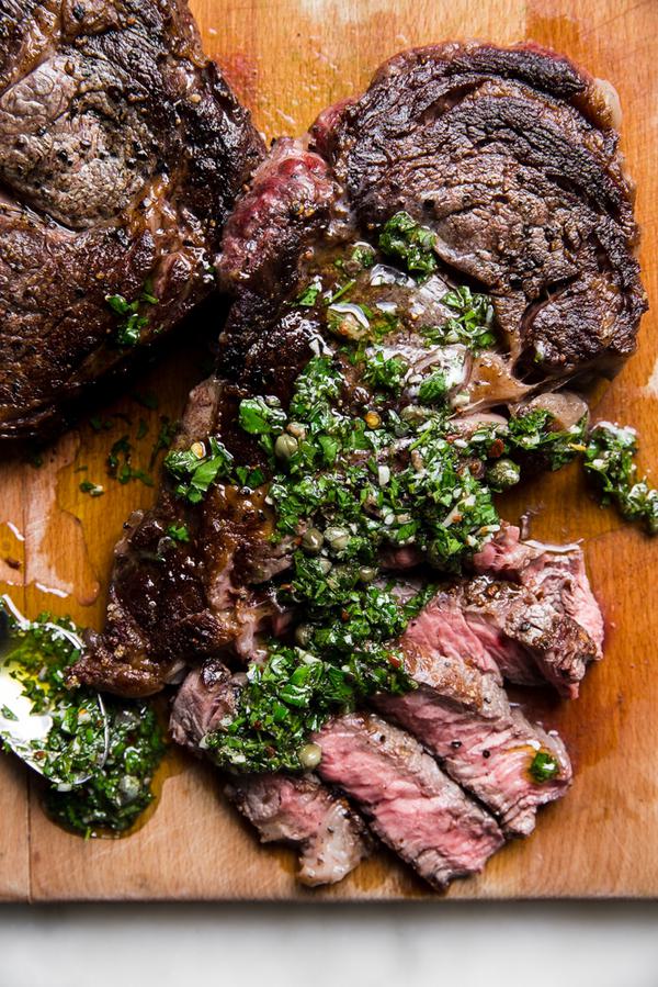Grilled ribeye steak sliced on a cutting board with salsa verde