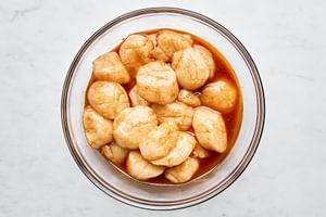 Raw sea scallops marinating in savory sauce in a glass bowl before grilling on a grill.