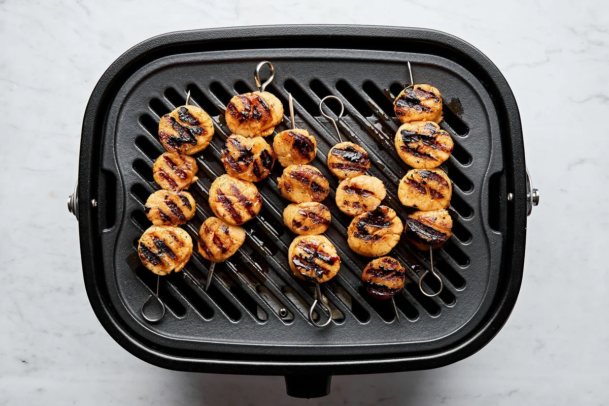 Grilled scallops cooking on an indoor electric grill pan showing perfect sear marks and caramelization.