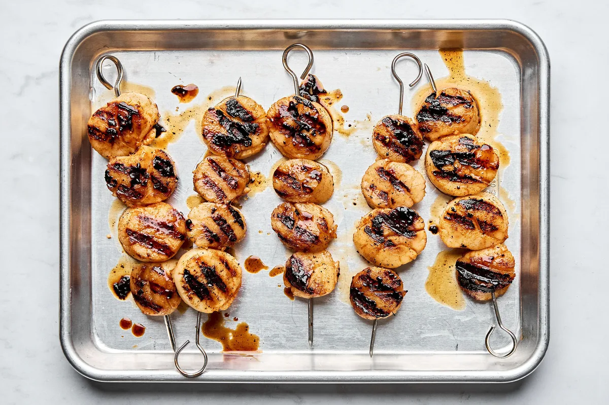 Finished grilled scallops on skewers on a rimmed sheet pan showing golden brown color and grill marks.