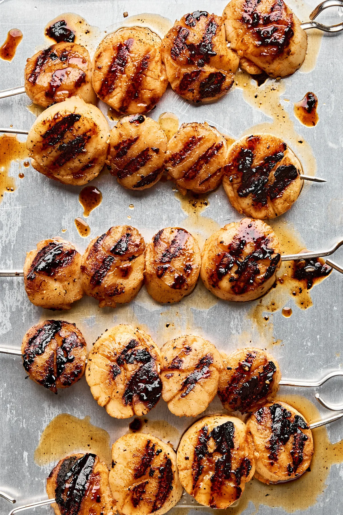 Close up shot of finished grilled scallops on skewers on a rimmed sheet pan showing golden brown color and grill marks.