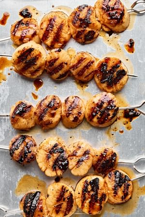 Close up shot of finished grilled scallops on skewers on a rimmed sheet pan showing golden brown color and grill marks.