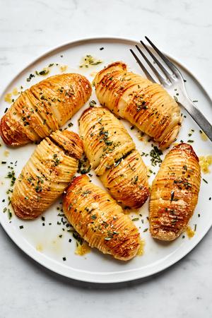 a platter of hasselback potatoes made with herb butter and topped with Parmesan and rosemary