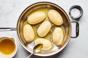 thinly sliced whole potatoes in a roasting pan being drizzled with herb butter
