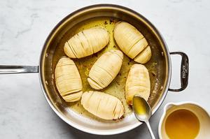 thinly sliced whole potatoes in a roasting pan being drizzled with herb butter