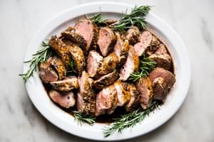 Herb crusted Pork Tenderloin with Port Wine Sauce on a white plate with rosemary