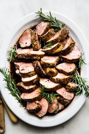 Herb crusted Pork Tenderloin with Port Wine Sauce on a white plate with rosemary