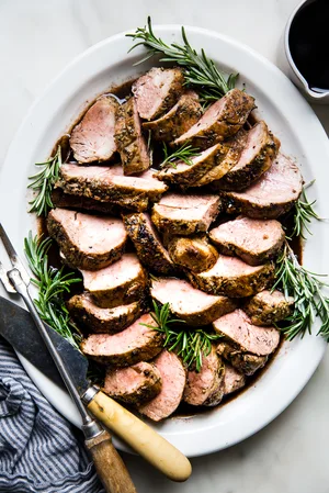 Herb crusted Pork Tenderloin with Port Wine Sauce on a white plate with rosemary