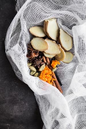 Ingredients for homemade Chai Tea concentrate in a cheese cloth fresh ginger, anise, cloves, cinnamon, cardamom, vanilla