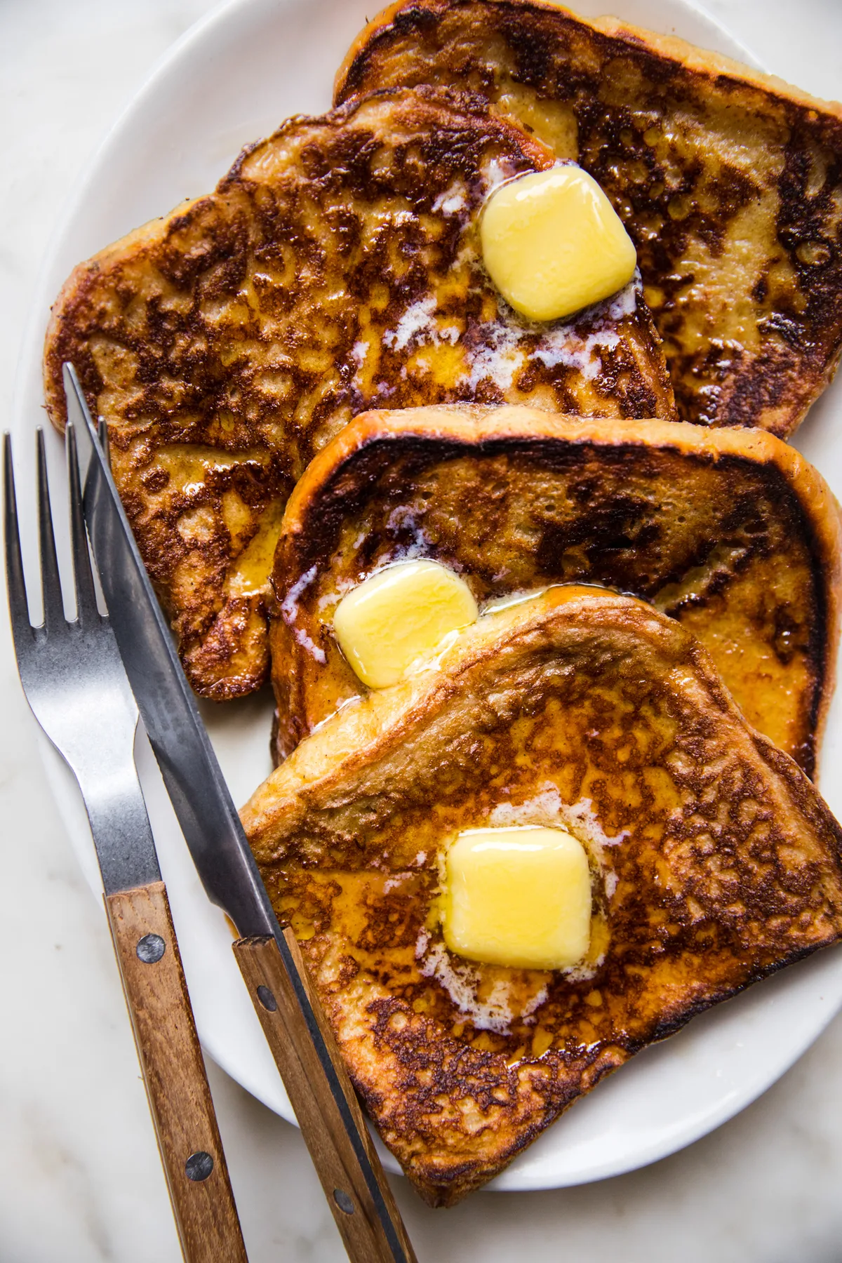 4 slices of homemade French toast topped with sliced butter and maple syrup in a list of the best breakfast recipes