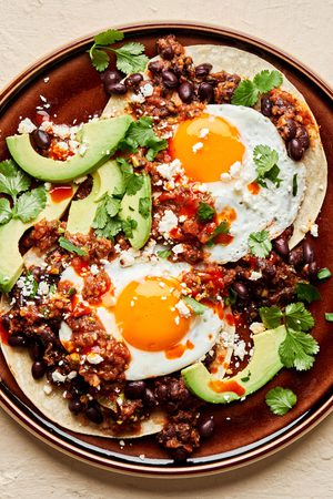 a plate of huevos rancheros topped with avocado and cilantro in a list of easy tex-mex brunch classic recipes