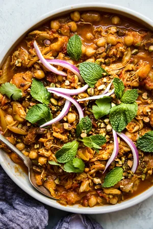 instant pot chicken tagine in a large white bowl topped with fresh mint and cilantro