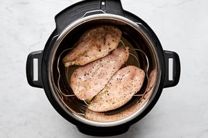 seasoned chicken breast on a rack in an instant pot with chicken broth, ready to make the easiest juicy chicken breast