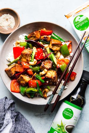 Kung pao with fried tofu, green onions and bell peppers in a bowl with rice and chop sticks. vegan and vegetarian kung pao