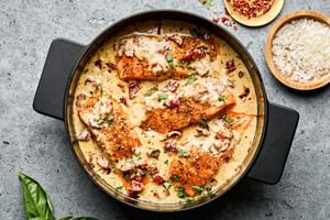 Marry Me Salmon fillets simmering in a creamy, sun-dried tomato sauce inside a skillet, garnished with basil and Parmesan.