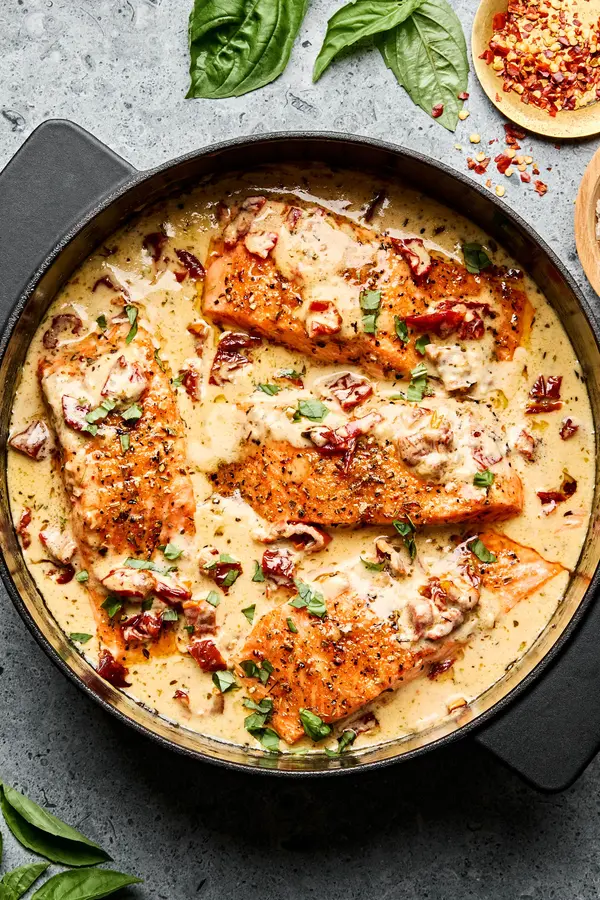 Marry Me Salmon fillets simmering in a creamy, sun-dried tomato sauce inside a skillet, garnished with basil and Parmesan.