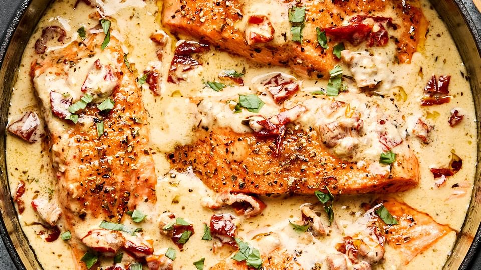 Marry Me Salmon fillets simmering in a creamy, sun-dried tomato sauce inside a skillet, garnished with basil and Parmesan.