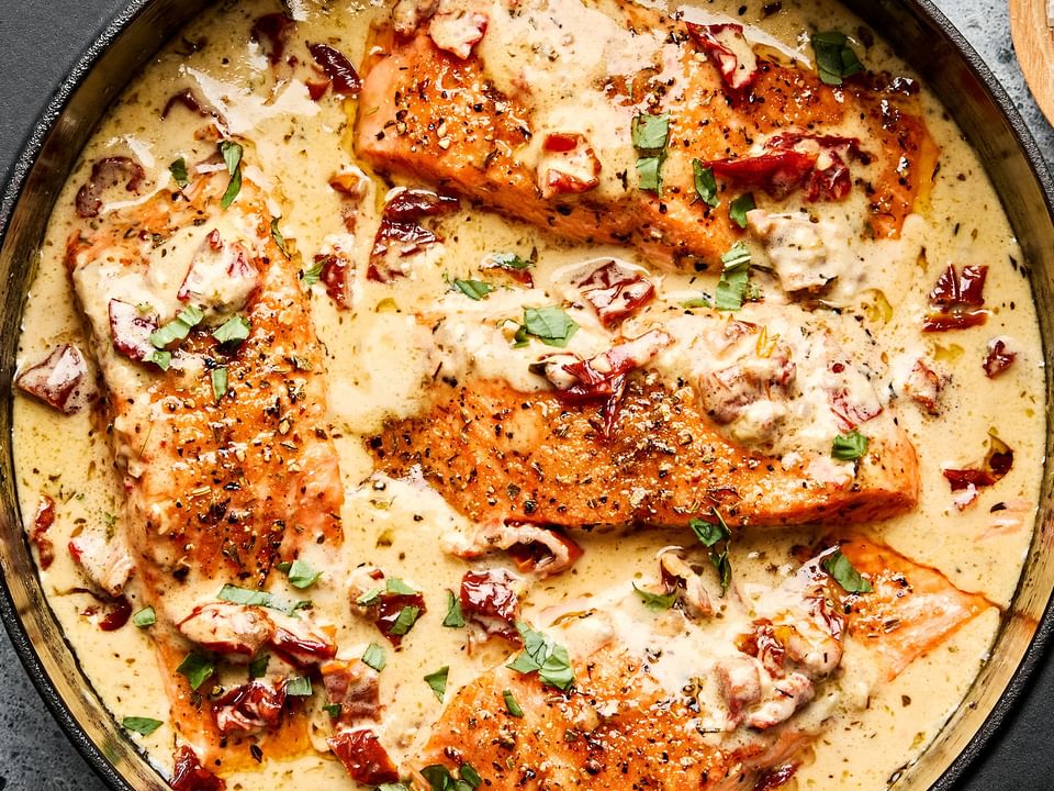 Marry Me Salmon fillets simmering in a creamy, sun-dried tomato sauce inside a skillet, garnished with basil and Parmesan.