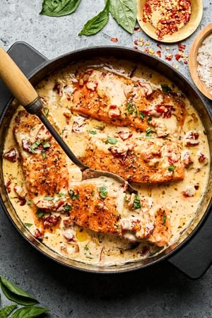 Marry Me Salmon fillets simmering in a creamy, sun-dried tomato sauce inside a skillet, garnished with basil and Parmesan.