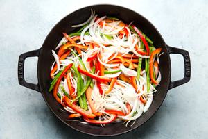 bell peppers and onions sliced thin cooking in a large black skillet