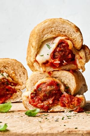 Golden brown meatball sub sandwiches, with marinara and melted cheese, sprinkled with parsley.