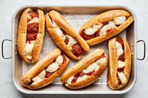 Golden brown meatball sub sandwiches, bubbling with marinara and melted cheese, fresh out of the oven on a baking sheet.