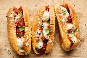 Golden brown meatball sub sandwiches, with marinara and melted cheese, sprinkled with parsley.