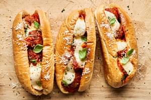 Golden brown meatball sub sandwiches, with marinara and melted cheese, sprinkled with parsley.