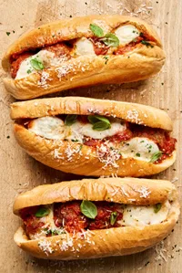 Golden brown meatball sub sandwiches, with marinara and melted cheese, sprinkled with parsley.