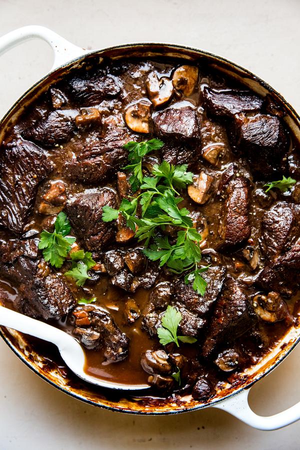 mushroom braised beef in a large white braiser topped with fresh parsley