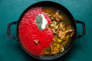 vegetables, mushrooms, spices, crushed tomatoes and red wine being cooked in a sauce pan for mushroom ragù