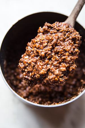 peanut butter and chocolatey no-bake cookie batter in a saucepan being stirred with a wooden spoon