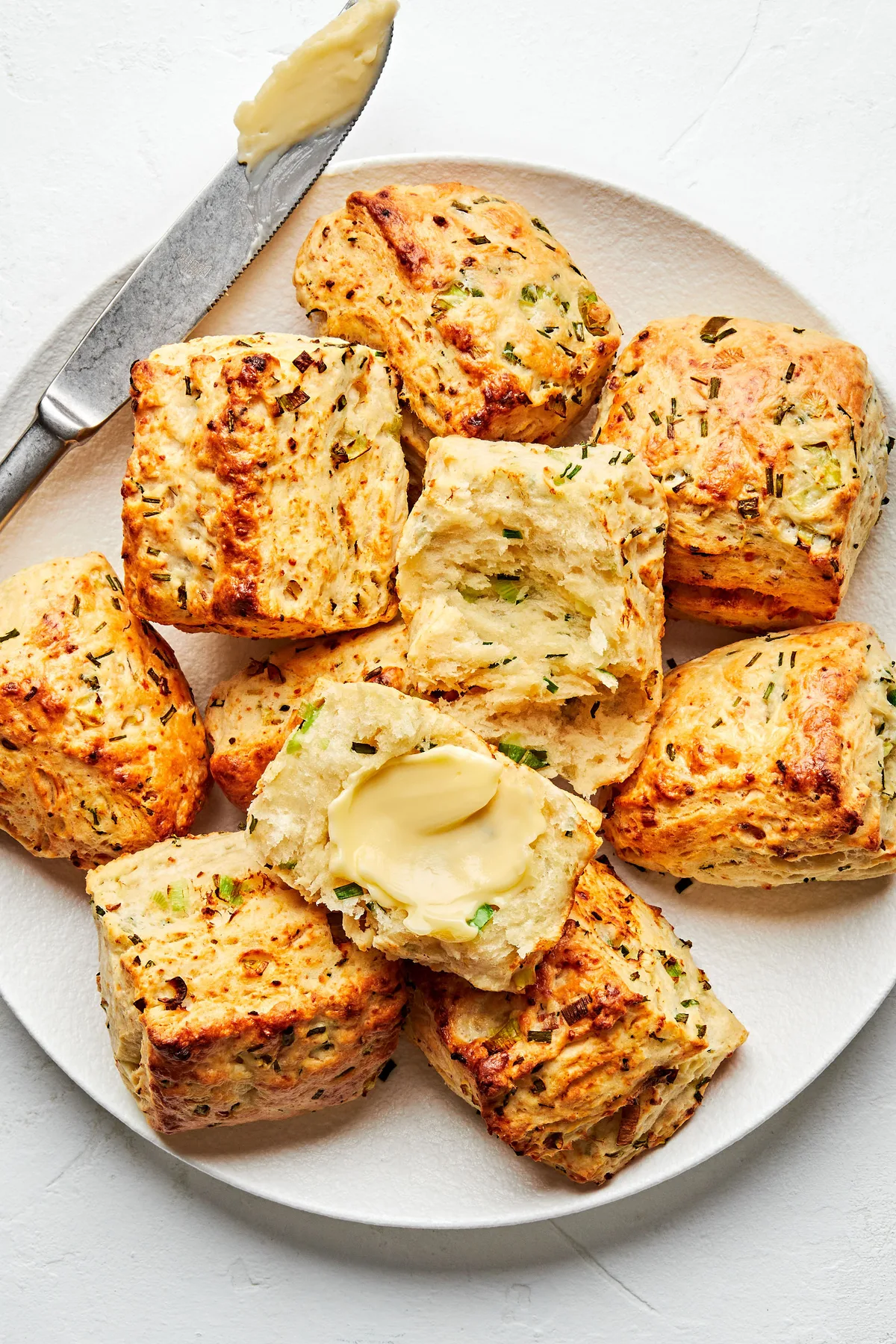 homemade onion chive biscuits being buttered on a plate in a list of best quick bread breakfast recipes