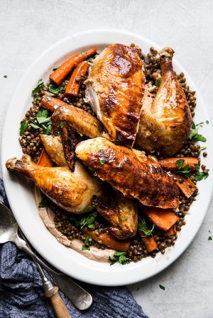 Roast chicken carved and shown on a bed of lentils with roasted carrots, parsley and a yogurt sauce.
