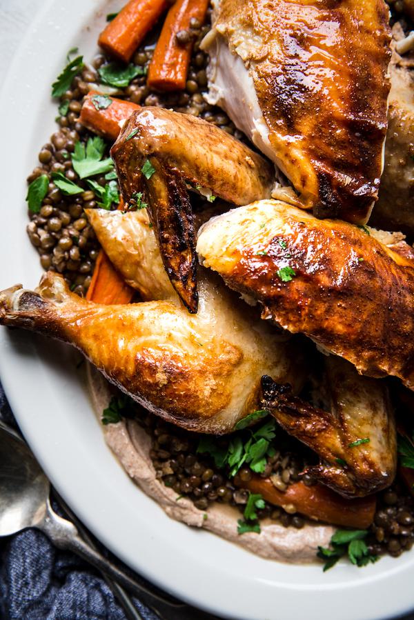 Paprika Roast chicken carved and shown over lentils and carrots on a white plater with a linen and a silver spoon.
