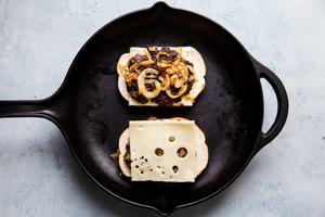 open face homemade patty melt topped with caramelized onions and swiss cheese being grilled in a skillet