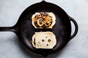 open face homemade patty melt topped with caramelized onions and swiss cheese being grilled in a skillet