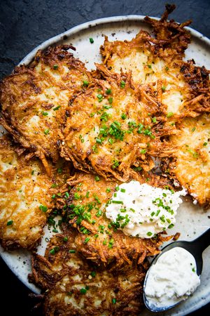 homemade potato pancakes on a plate topped with a dollop of sour cream in a of the best breakfast potato dish recipes