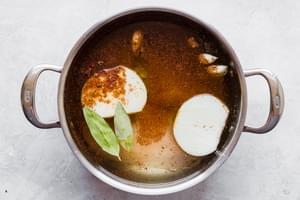Large stainless steal pot with spices, onions, bay leaves and chicken breasts