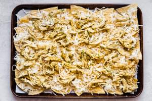 shredded cheese and salsa verde chicken on top of corn chips for nachos
