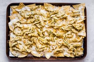 melted cheese and and cooked chicken on chips shown on a baking dish