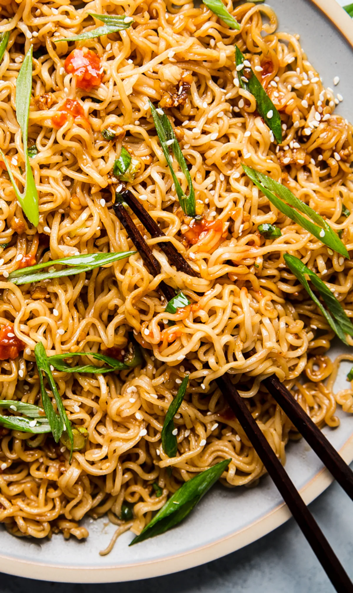 a plate of sesame garlic ramen noodles topped with green onions and sesame seeds with chopsticks