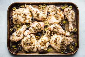 raw chicken marbella on a sheet pan with olives and prunes