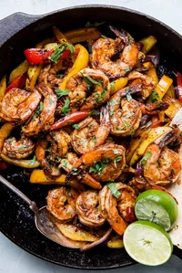 shrimp fajitas in a cast iron skillet with limes and bell peppers