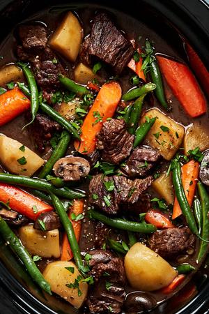 a crock pot full of slow cooker beef stew made with potatoes, green beans, carrots, onions and celery