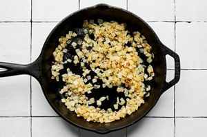 chopped onion being cooked in olive oil in a cast iron skillet to be used on top of smash burgers