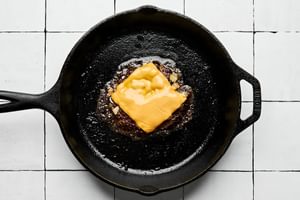 a smash burger cooking in a cast iron skillet topped with chopped cooked onions and melty american cheese