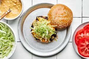 smash burger on a toasted bun, layered with crisp lettuce, cooked onion, melted American cheese, and a slice of fresh tomato