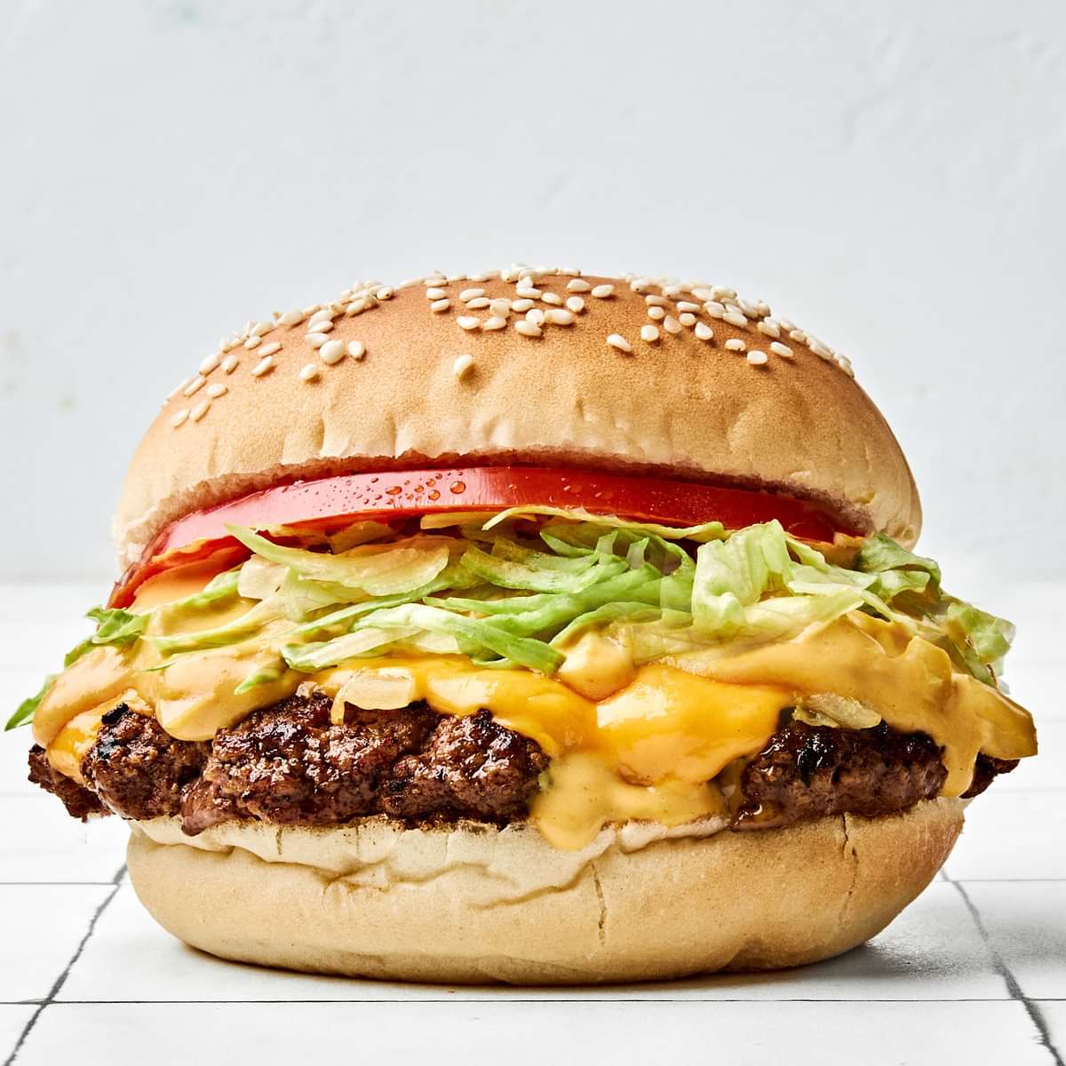 smash burger on a toasted bun, layered with crisp lettuce, cooked onion, melted American cheese, and a slice of fresh tomato